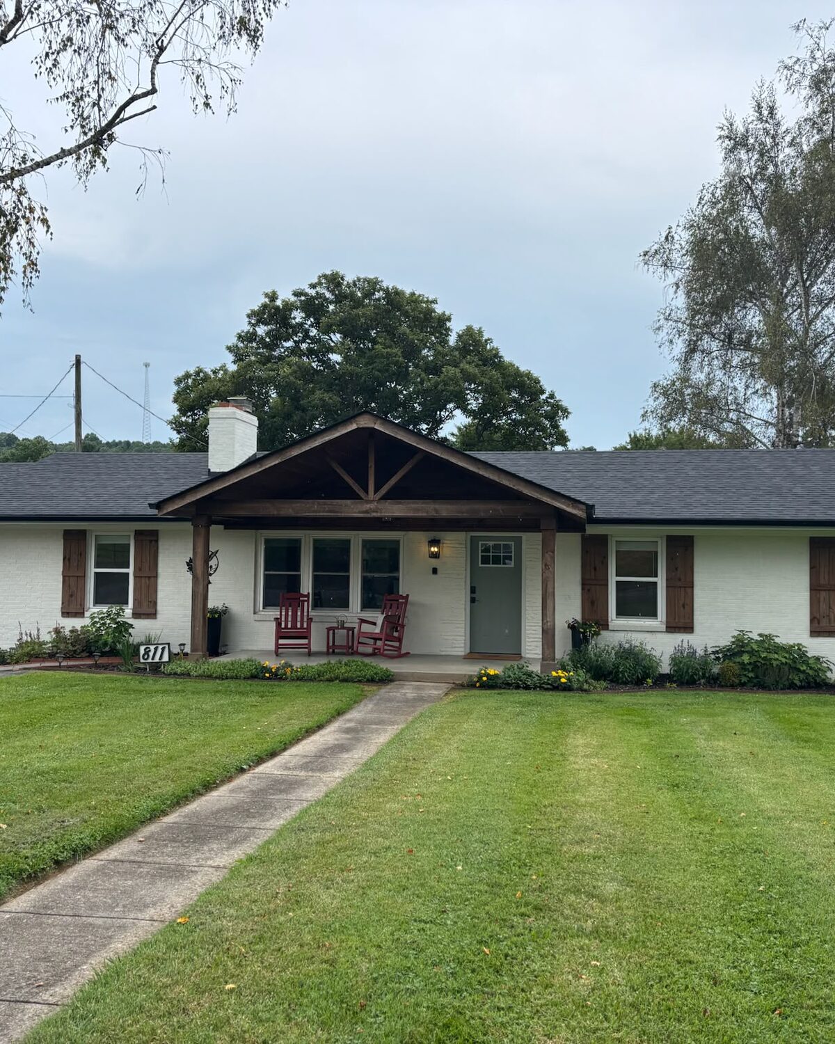 The house's white painted-brick exterior and covered front porch, seen across the lawn with the walkway leading up to the entrance.