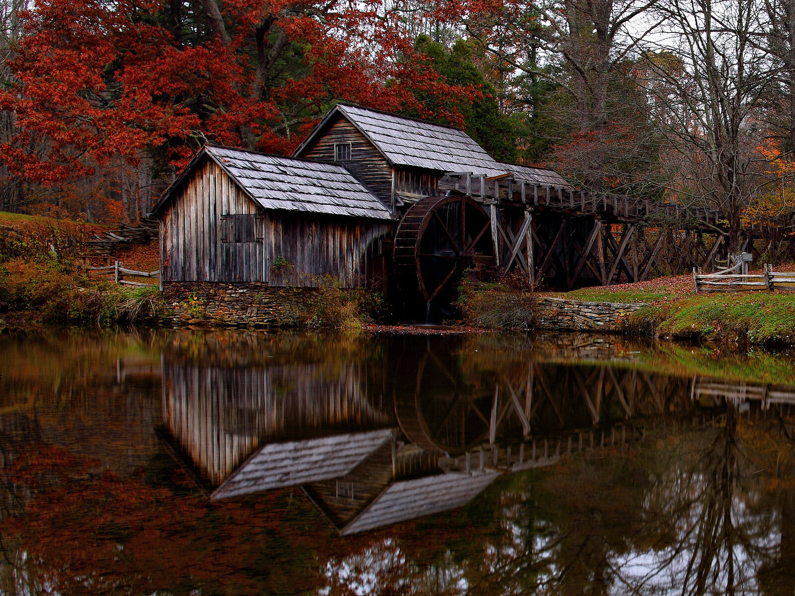 Mabry Mill's water wheel and wooden gristmill reflected in its still pond, surrounded by red and orange fall foliage.