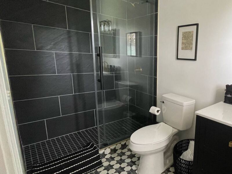 A bathroom with a black-tiled walk-in shower behind a glass door, and a black-and-white patterned tile floor.