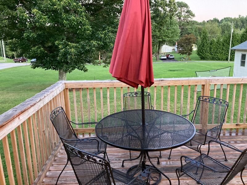 The timber deck with a round mesh patio table, wrought-iron chairs and a red umbrella, looking out over the lawn.