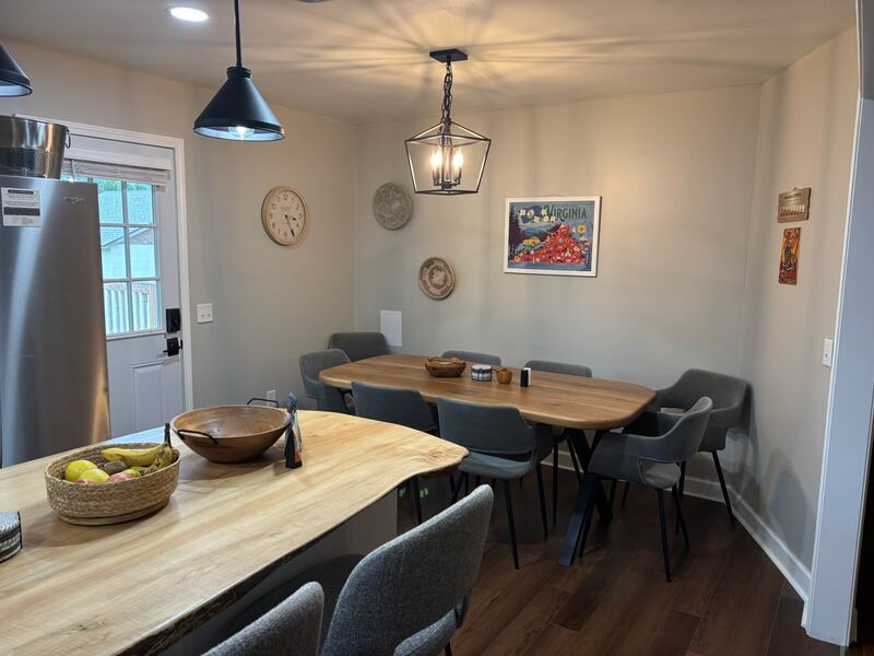The dining table in live-edge wood, seating eight, under a lantern-style pendant, with a Virginia travel poster on the wall.