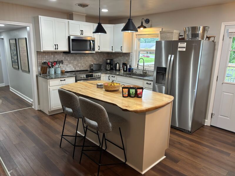 The live-edge wood island with upholstered bar stools, beneath two black cone pendant lights.