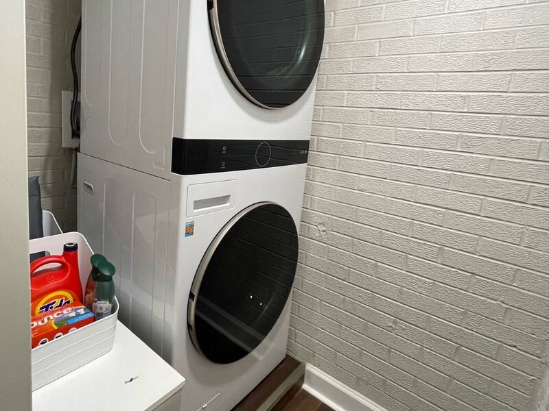 A stacked washer and dryer set into an alcove lined with painted white brick.