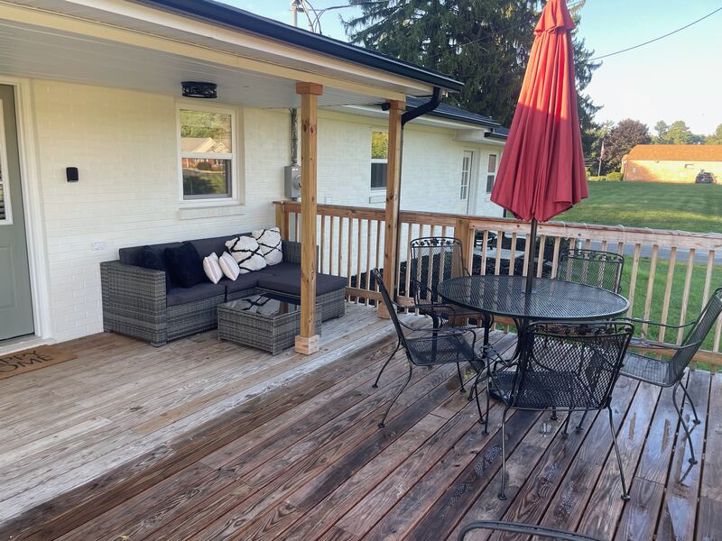 The covered back porch, with a wicker corner sofa and cushions, opening onto the deck's table and chairs beyond.